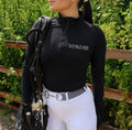 Female rider wearing black long sleeve baselayer with silver Mane Equestrian logo