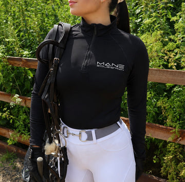 Female rider wearing black long sleeve baselayer with silver Mane Equestrian logo