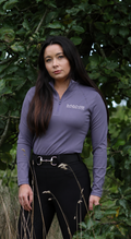 Woman wearing a purple equestrian shirt with a logo in front of green foliage