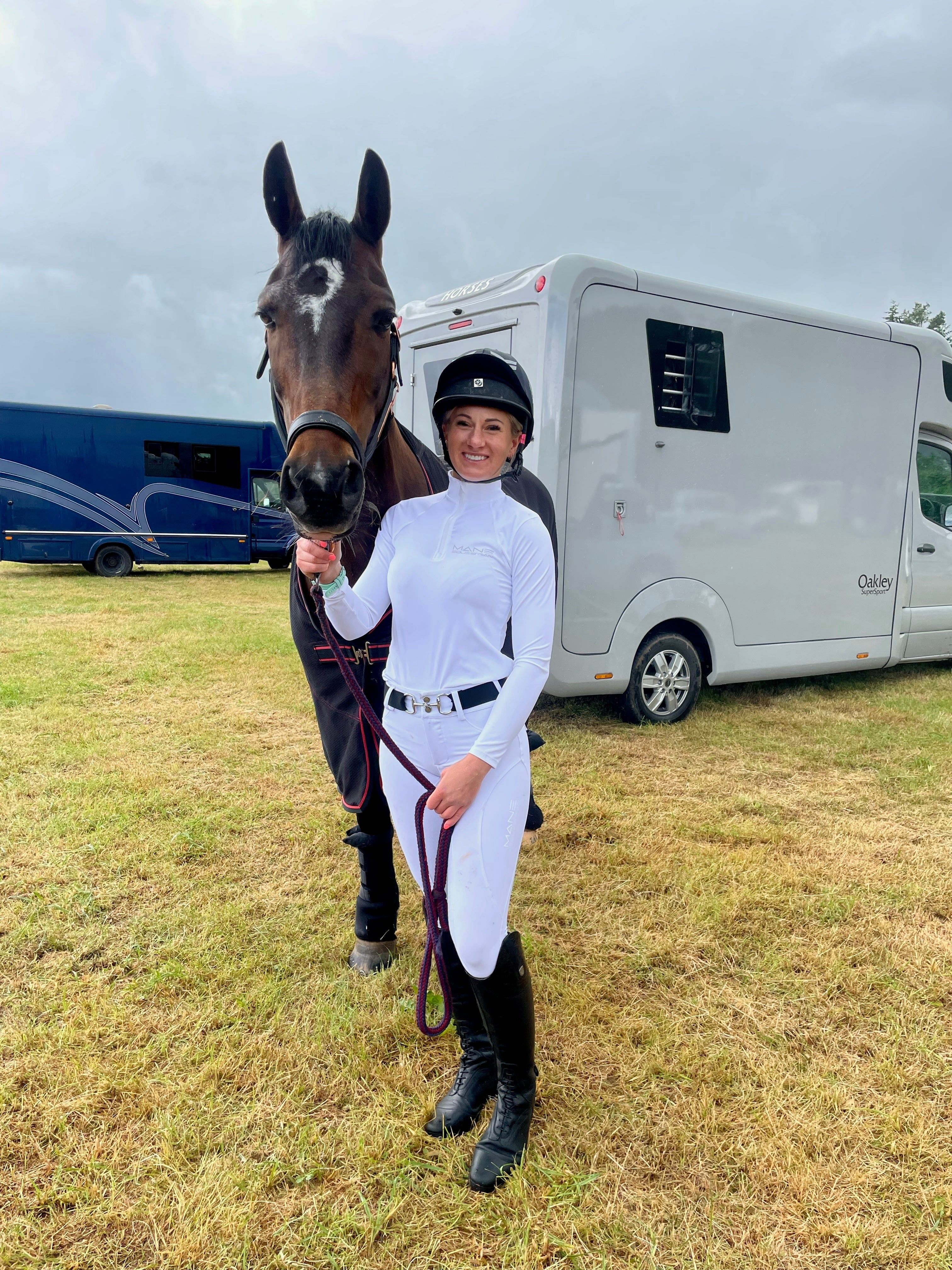 A person riding a horse wearing a white long sleeved baselayer and white long riding trousers. The person is wearing black riding boots and a black belt.