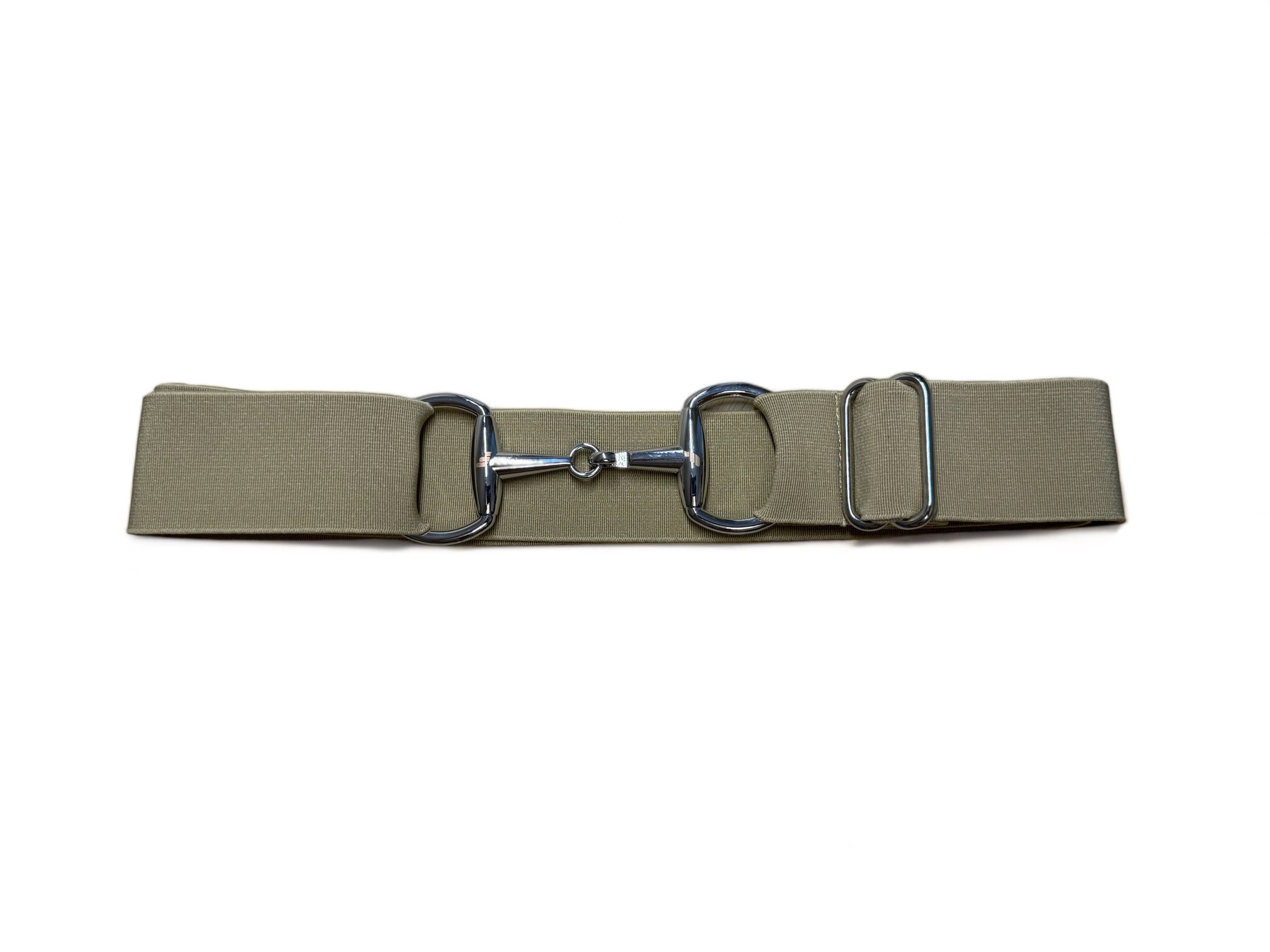 A person wearing a brown turtleneck top and a white belt with a silver snaffle design holding on a brown saddle.