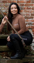 A person wearing a chestnut baselayer with black performance breeches sat on steps against a brick wall