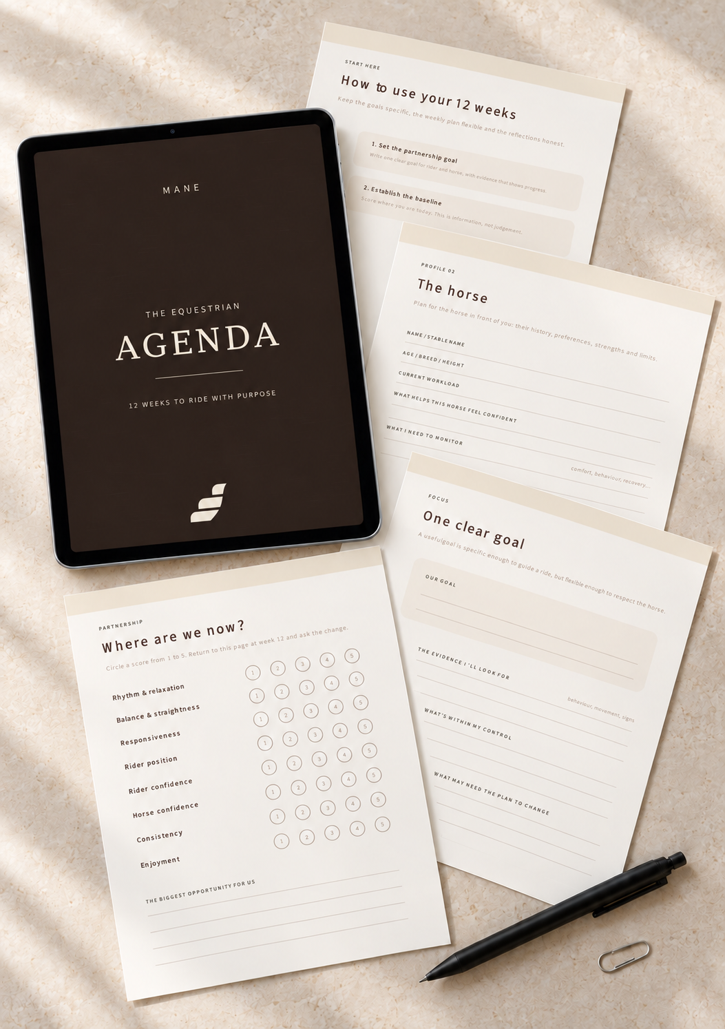 A digital planner template displayed on a tablet screen with several printed worksheet pages fanned out behind it, plus a black pen and paperclip on a soft beige fabric background. The tablet cover reads 'MANE THE EQUESTRIAN AGENDA'.