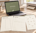 A laptop on a sunlit desk displays an agenda screen, with printed agenda sheets spread out in front. The scene includes a printer, cup with pens, and a window in the background, creating a styled workspace setup.